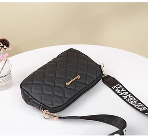 Detail of black quilted camera bag with gold logo and wide crossbody letter strap