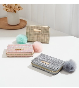 Detailed view of woven mini wallets in pink, green, and gray with fluffy pompom charms