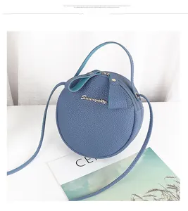 Close-up of blue circular crossbody bag with litchi grain texture and golden metal logo
