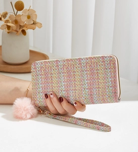 Détail d'une pochette tissée colorée avec pompon rose et dragonne de poignet amovible