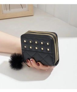 Gros plan d'un mini porte-monnaie matelassé noir avec rivets dorés et pompon doux
