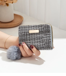 Close-up of grey woven tweed wallet with golden logo plate and fluffy pom-pom charm