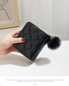Détail d'un mini porte-monnaie matelassé noir avec zip doré et breloque pompon en peluche