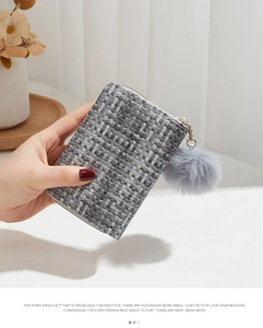 Close-up of gray woven texture small wallet with matching pompom and gold zipper