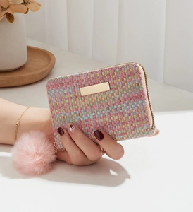 Detail of colorful woven tweed wallet with gold zipper and pink faux fur pompom charm