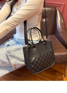 Detail of black quilted tote bag with dual handles and adjustable woven shoulder strap