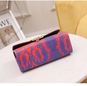 Detail of red and blue gradient snakeskin texture with a round gold metal clasp