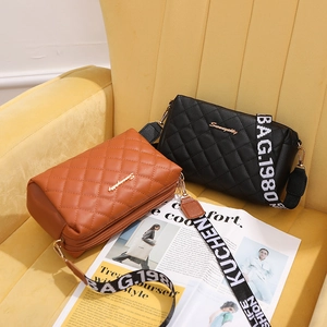 Quilted cross-body bags in black and brown with embroidered wide straps on a velvet chair