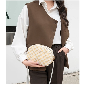 Détail d'un sac bandoulière ovale beige avec motifs floraux jaunes et fermoir papillon