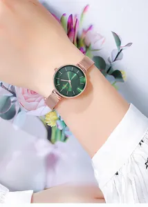 Close-up of rose gold mesh watch with deep green sunburst dial on a floral background