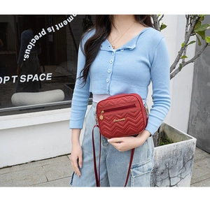 Détail d'un sac bandoulière rouge matelassé avec surpiqûres en V et finitions dorées