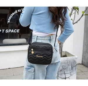 Détail des surpiqûres ondulées et du logo en métal doré sur le sac bandoulière noir