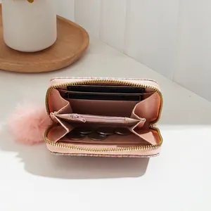 Pink woven fabric card holder wallet with a gold zipper and decorative plush ball charm