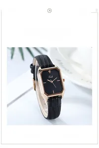 Detail of rose gold rectangular watch case with black leather strap on a minimalist desk
