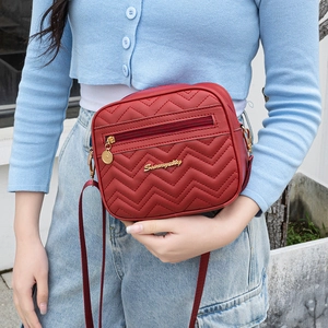 Sac bandoulière rouge avec texture matelassée en V et logo doré porté par un mannequin