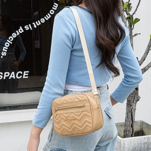 Sac bandoulière beige matelassé avec motif chevron et sangle ajustable porté par un mannequin