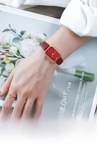 Close-up of a square rose gold watch with red sunray dial and matching leather strap