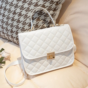White quilted shoulder bag with gold twist lock and top handle on a beige cushion