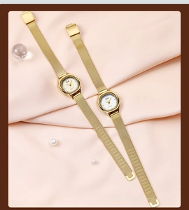 Detailed close-up of a golden mesh strap watch on silk with pearl and glass accents