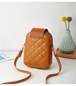 Caramel quilted crossbody phone bag on a wooden tray with a minimalist vase