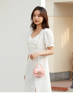 Pink mini jelly bag with chain strap and studded detail worn by a model in a white dress