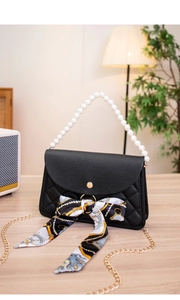 Detailed view of black quilted bag with pearl handle, silk scarf, and gold-tone clasp