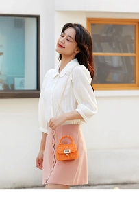 Close-up of orange mini jelly bag with rivet texture, woven handle and gold chain strap