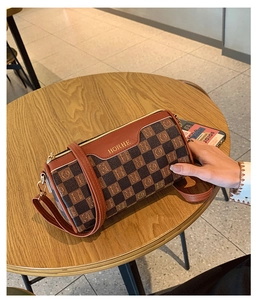 Detailansicht der karierten Zylindertasche mit goldenen Beschlägen und Lederriemen