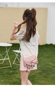 Detail of pink quilted crossbody bag with pearl chain and silk scarf on a model