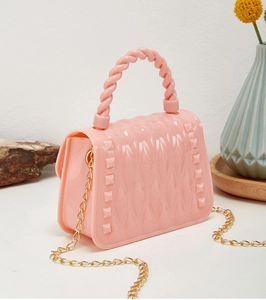 Pink jelly mini bag showing golden chain strap and stud details on a textured wooden tray