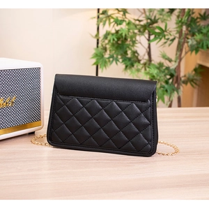 Close-up of black quilted leather crossbody bag with golden chain strap on a desk