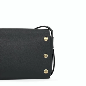 Detail shot of black leather handbag featuring vertical gold metal rivets and fine texture