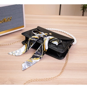 Detail of black quilted leather handbag featuring a pearl handle and decorative silk scarf