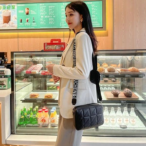 Sac bandoulière chic en cuir matelassé noir avec large sangle lettrée porté par un mannequin