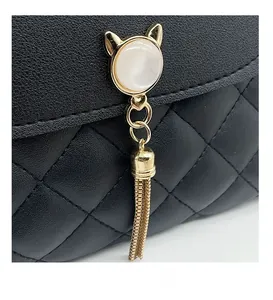 Detail of black quilted leather handbag with gold cat-ear hardware and metal tassels