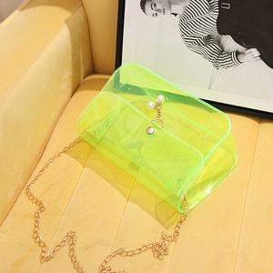 Neon green clear PVC shoulder bag with gold chain and pearl embellishments on a sofa