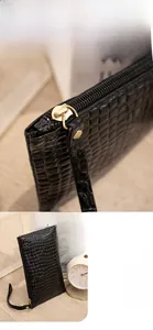 Detail of smooth gold metal zipper on black crocodile texture clutch bag with wristlet