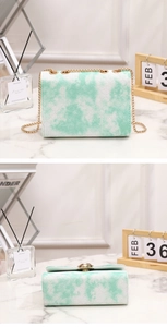 Detail of mint green tie-dye chain bag with gold hardware on marble surface