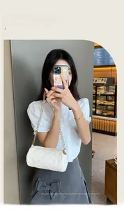Detail of white quilted cylinder bag with gold chain strap held in a cafe setting