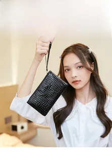Detail of a black crocodile-embossed clutch bag held by a model with a wrist strap