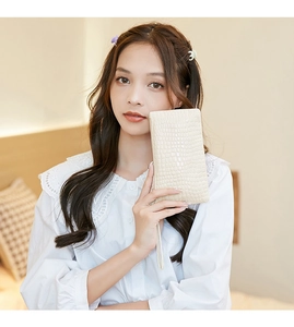 Close-up of a beige faux crocodile embossed clutch bag with wristlet strap held by model