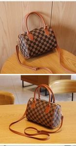 Close-up of checkerboard Boston bag with gold zipper and leather handles on wooden surface