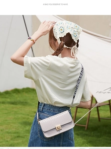 Close-up of woven square crossbody bag with gold buckle and lettered canvas strap