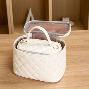White quilted cosmetic bag set with gold zippers and nested pouch on wooden table