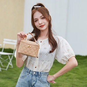 Elegant beige quilted vanity handbag with top handle and dual zipper on outdoor background