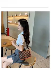 Bolso bandolera de cuadros marrones con logo HORHE lucido por modelo sentada