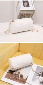 Detail of white quilted cylindrical crossbody bag with gold chain strap on soft yellow fabric