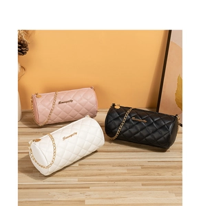 Three quilted cylinder chain bags in pink, white, and black on a wooden table with decor