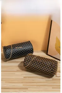Close-up of black and brown quilted cylinder bags with gold chain straps on a wooden table