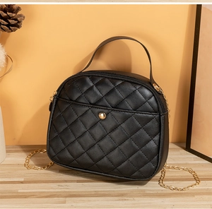 Detail of black quilted crossbody bag with gold chain and circular clasp on wood table